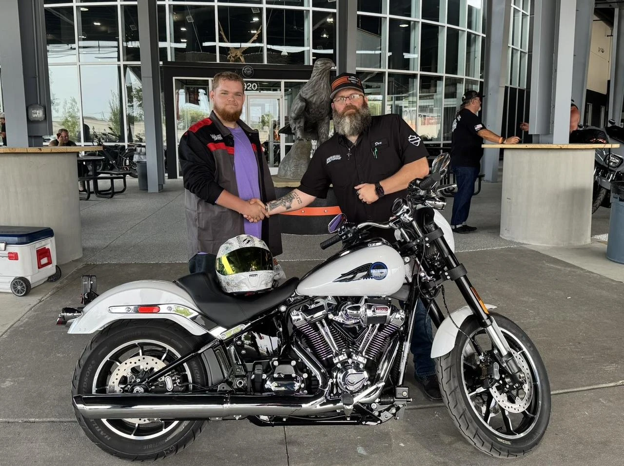 Two men shake hands beside a Harley-Davidson motorcycle at a dealership, Aug. 22, 2026. (Photo via X/@AEHD_KickAss)