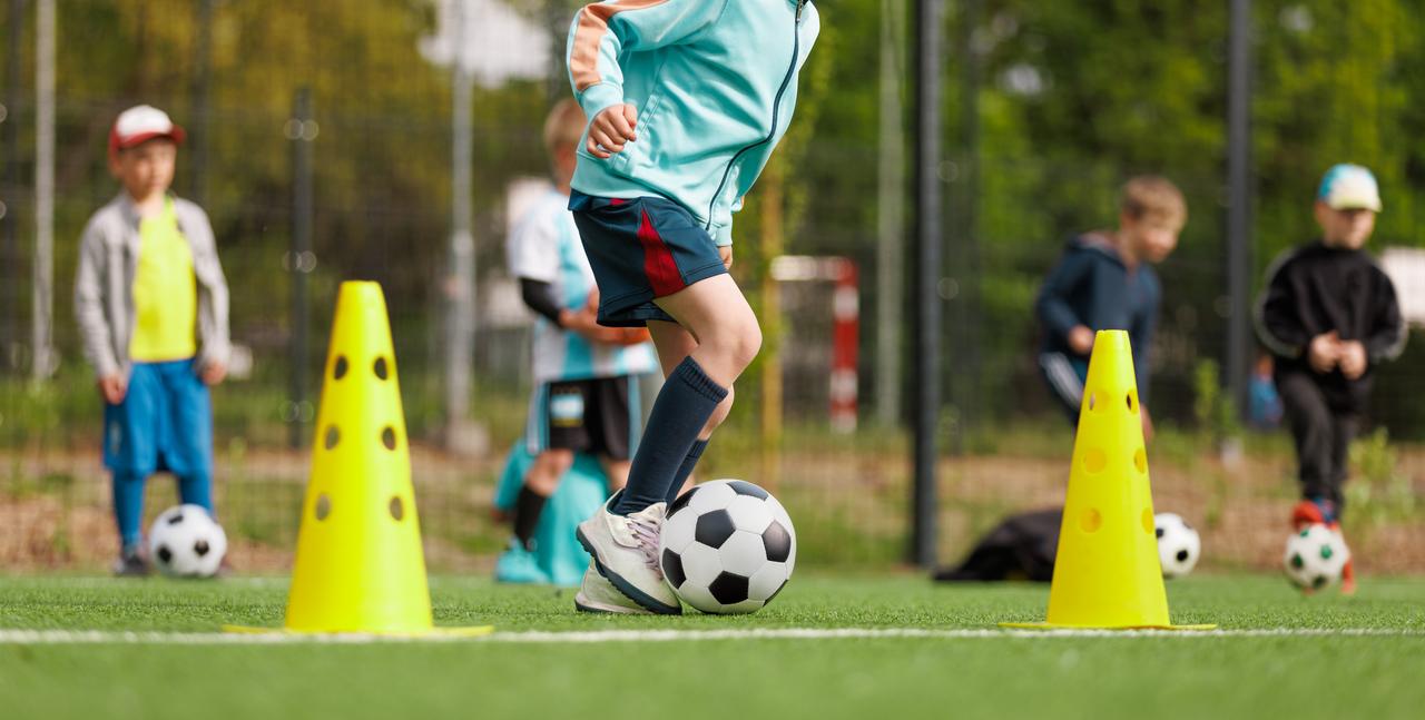 A child practices ball control between training cones during a youth soccer session outdoors. (Adobe Stock Photo)