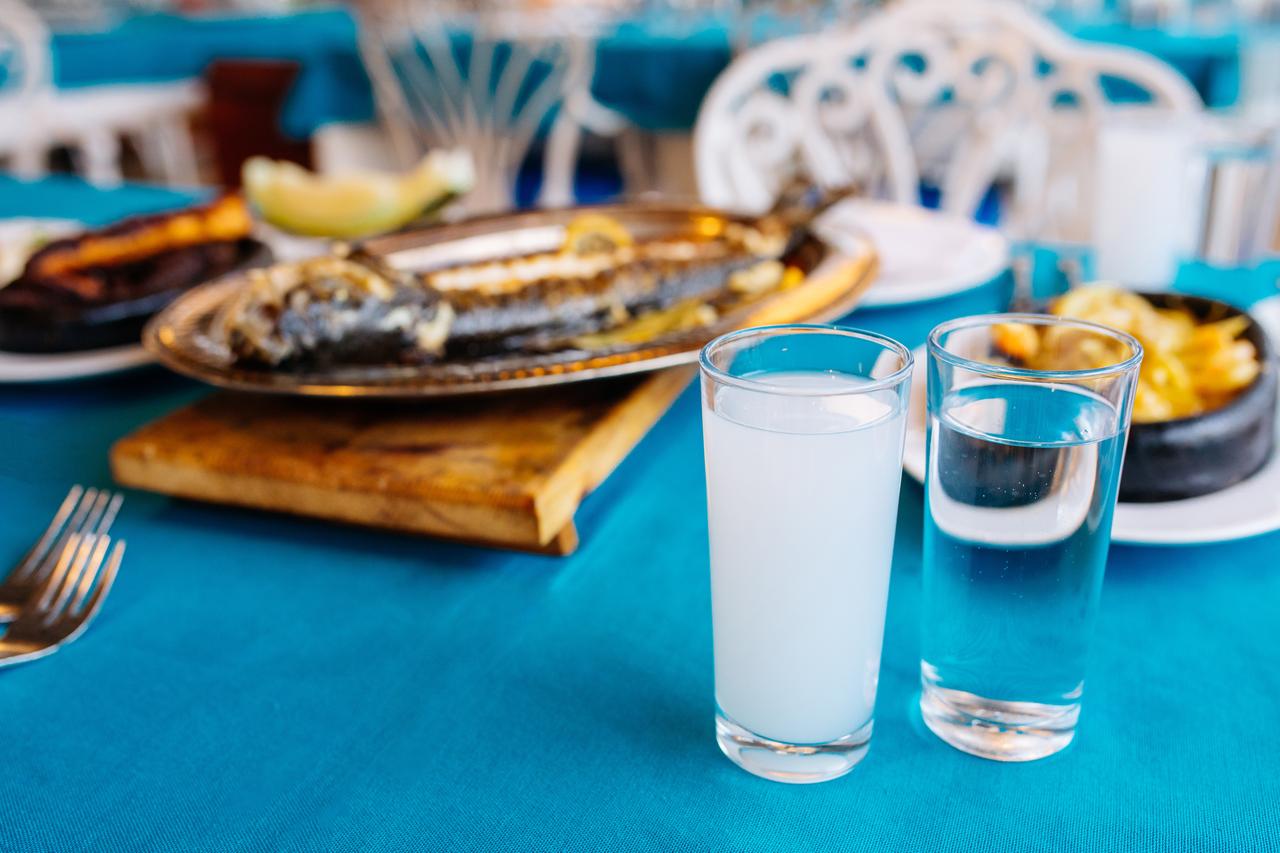 Raki gone milk-white with water, grilled fish waiting behind it—the table's usual order of operations. (Adobe Stock Photo)