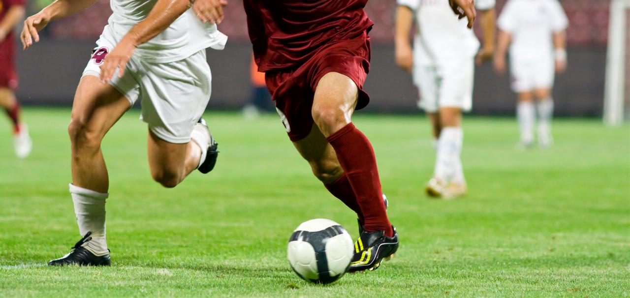 Football players compete for possession during a match on a grass pitch. (Adobe Stock Photo)