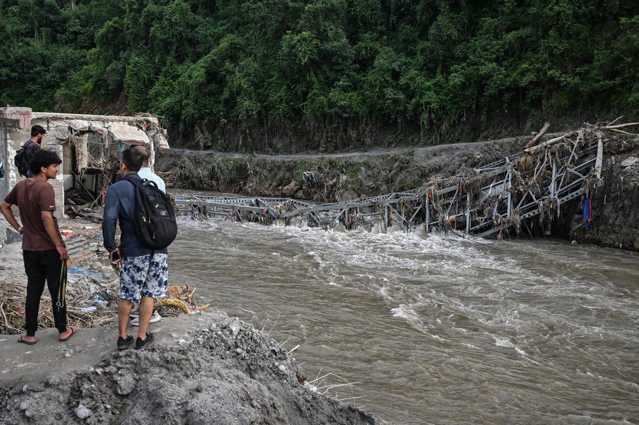 People stand near a collapsed bridge after flash floods in Devighat, Nepal, Aug. 28, 2026. (AFP Photo)