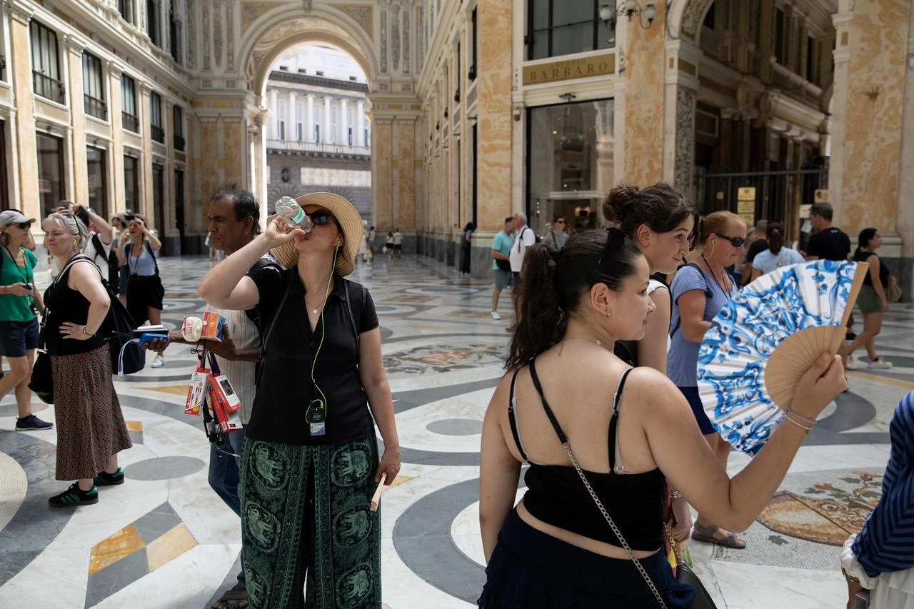 People use umbrellas, hand fans, and hats to protect themselves from the sun; they drink cold beverages to cool off during a warm afternoon in Naples, Italy, Aug. 01, 2026. (AA Photo)