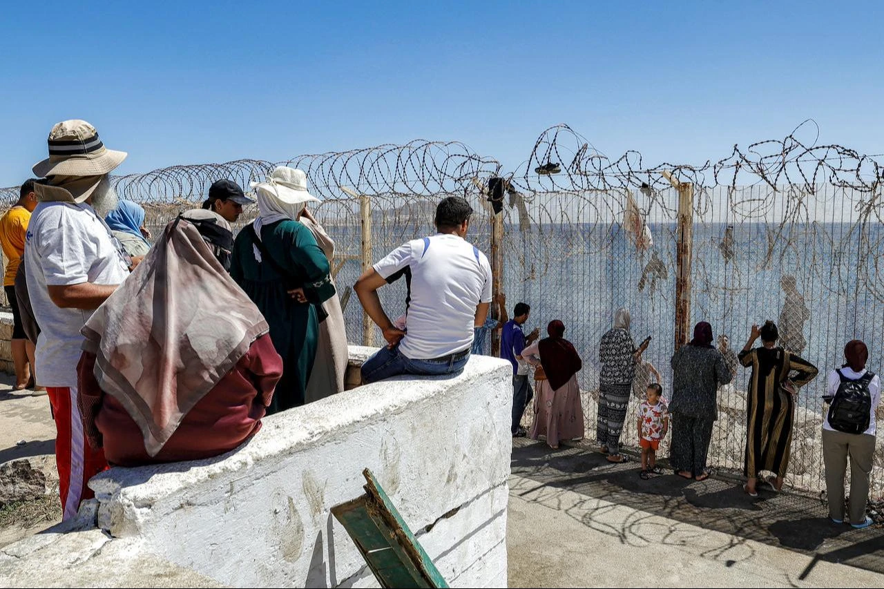 Relatives and friends wait by a fence topped with barbed wire for the return of people who had previously crossed into Spain's North African enclave of Ceuta, at Morocco's Bab Sebta border crossing on the outskirts of Fnideq, August 2, 2026. (AFP Photo)