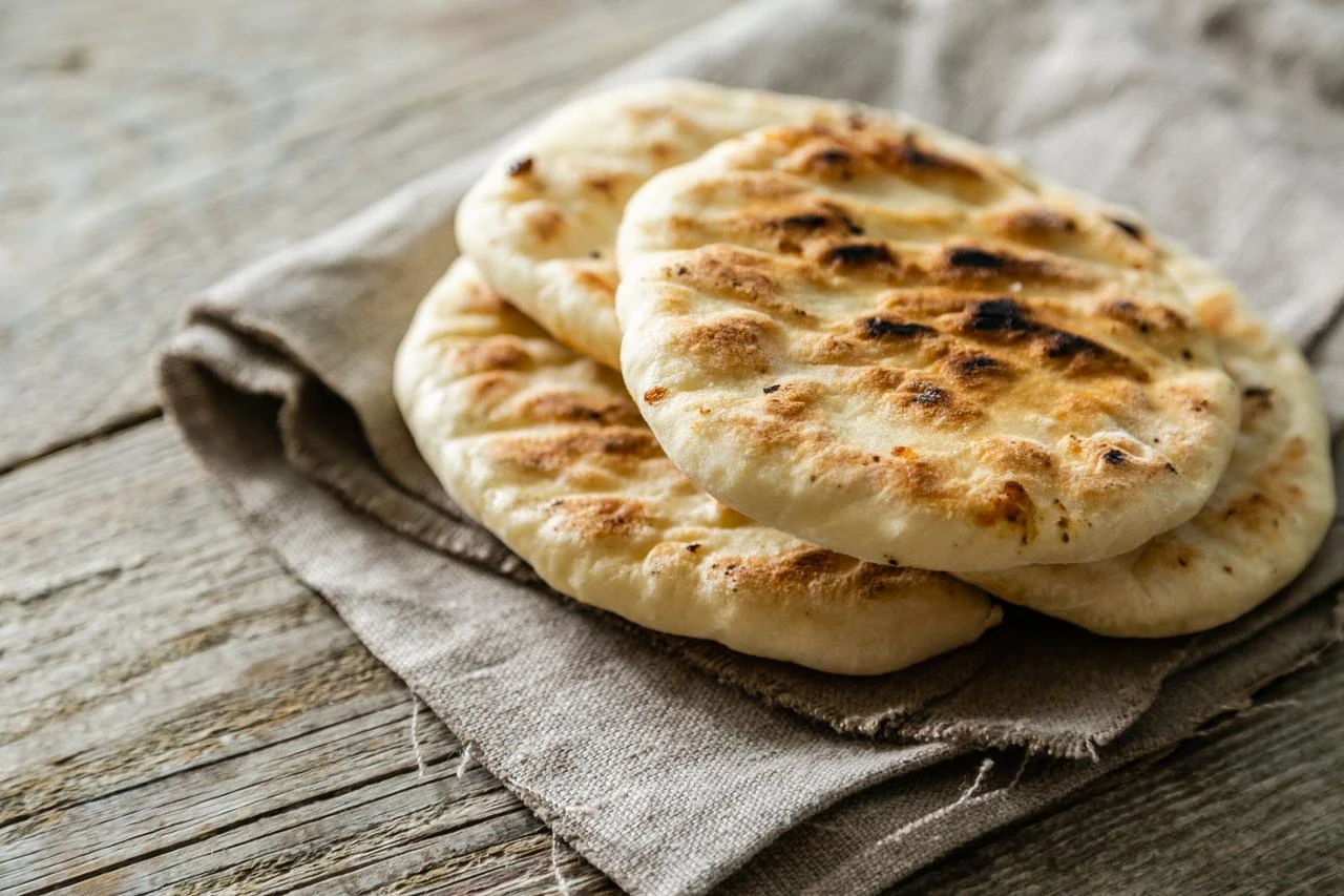 A stack of freshly baked pita flatbreads rests on a rustic wooden table. (Adobe Stock Photo)