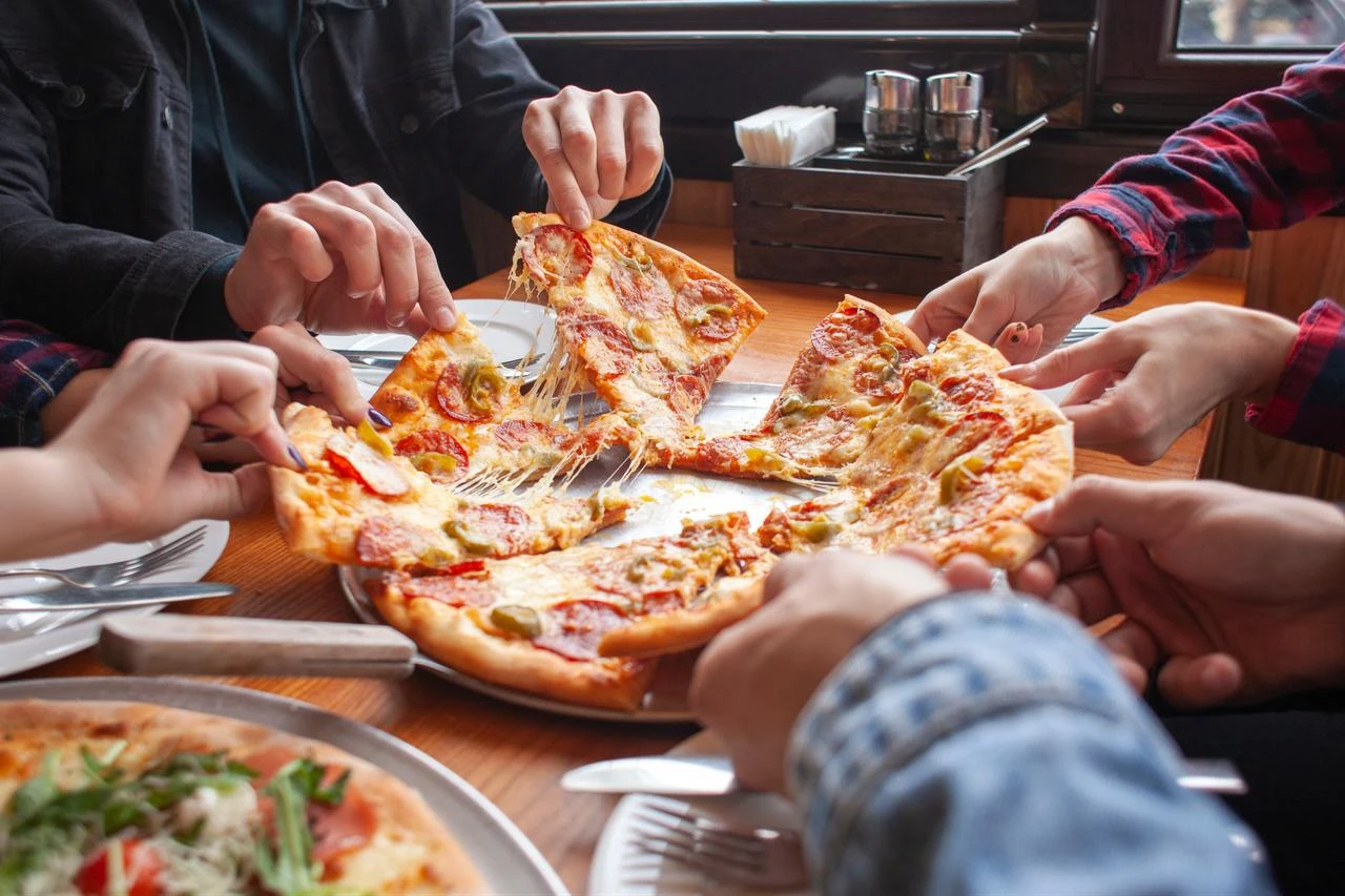 Group of students friends eat Italian pizza, hands take slices of pizza in a restaurant. (Adobe Stock Photo)