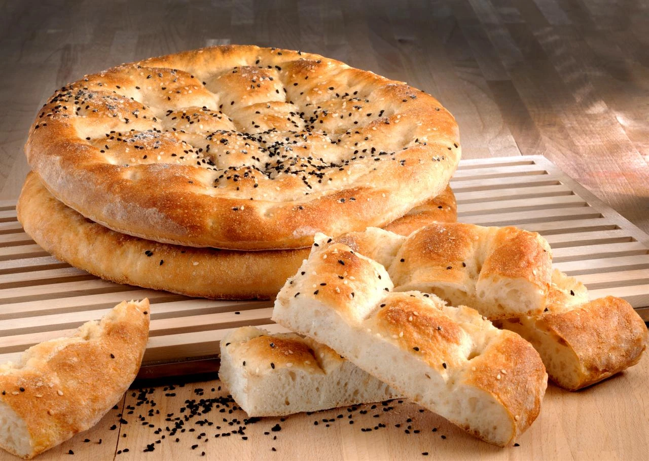 Freshly baked Ramadan pide, topped with sesame and nigella seeds, is sliced and served on a wooden board. (Adobe Stock Photo)