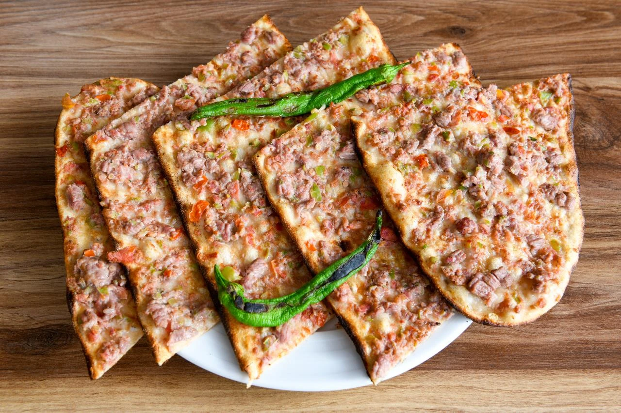 Freshly baked minced-meat pide is sliced and served with roasted green peppers on a wooden table. (Adobe Stock Photo)
