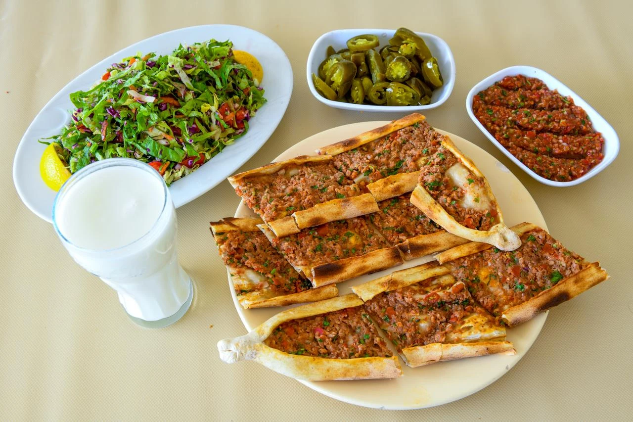 Minced-meat pide is served with ayran, salad, pickled peppers and a spicy tomato-based side dish. (Adobe Stock Photo)