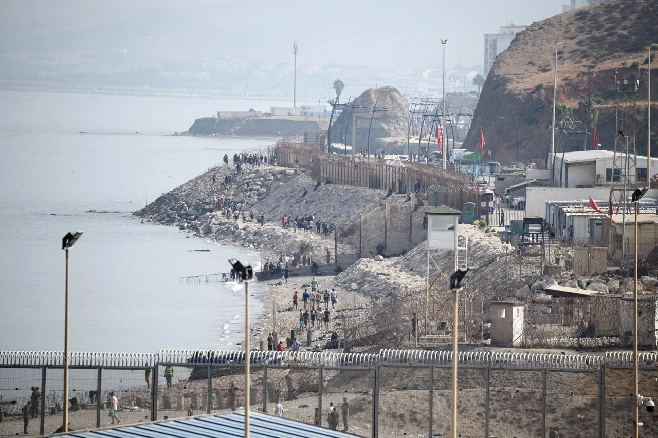 Migrants walk along the shoreline near the border fence separating Morocco and the Spanish North African enclave of Ceuta as they return to Morocco, as seen from Ceuta, August 1, 2026. (AFP Photo)