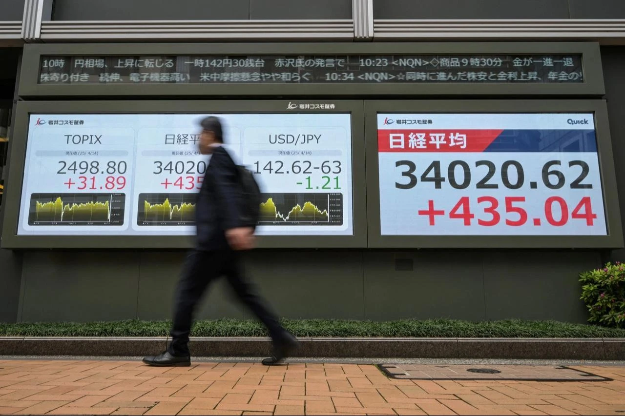 A man walks past an electronic board showing the Japanese yen/US dollar exchange rate (C) and the numbers of morning trading (R) on the Tokyo Stock Exchange along a street in Tokyo, April 14, 2025. (AFP Photo)