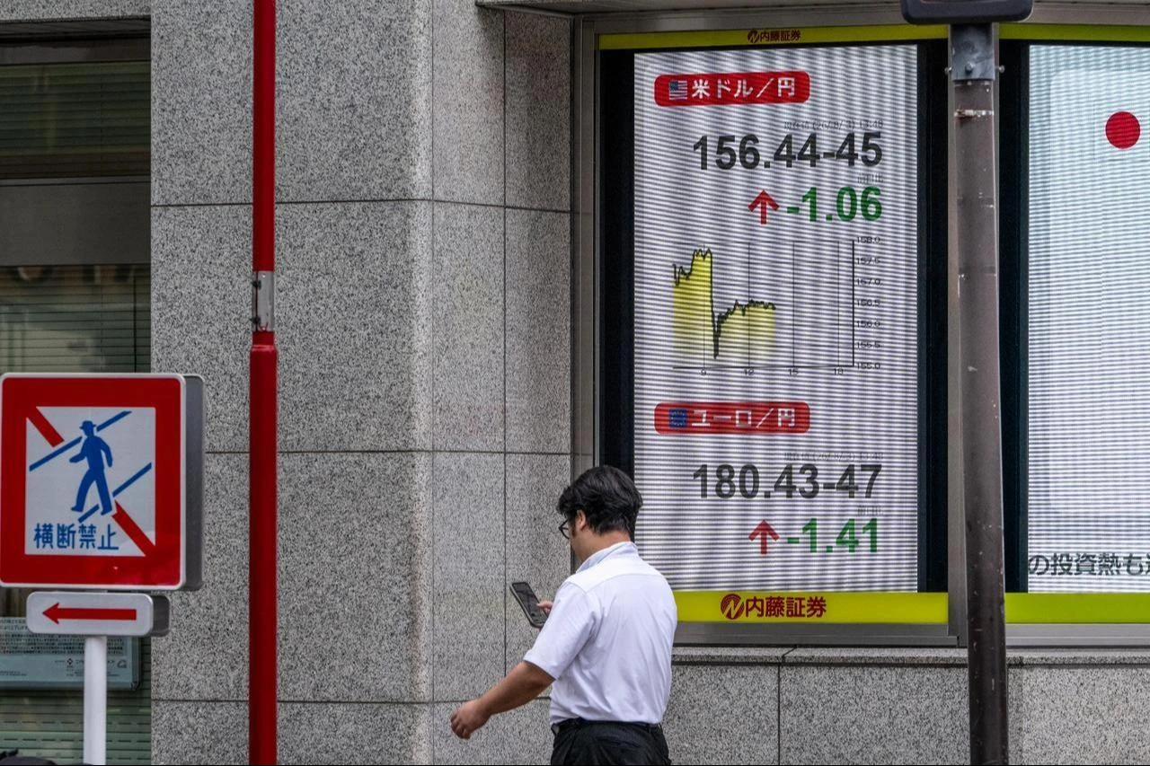 A man checks his phone next to a board showing the US dollar and Japanese yen exchange rate at a securities firm in Tokyo, August 3, 2026. (AFP Photo)