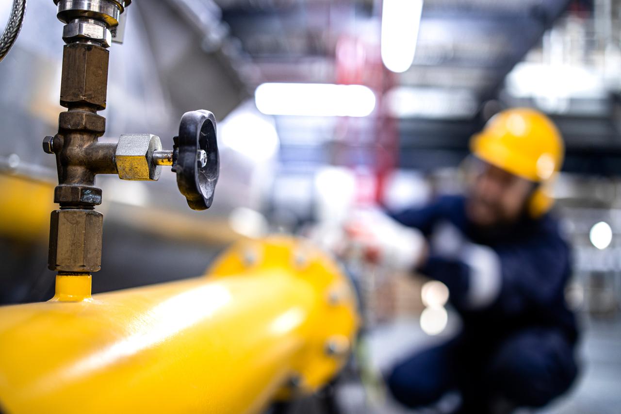 Close up view of natural gas pipeline with valve and refinery worker working in the background, accessed on Aug. 31. 2026. (Adobe Stock Photo)