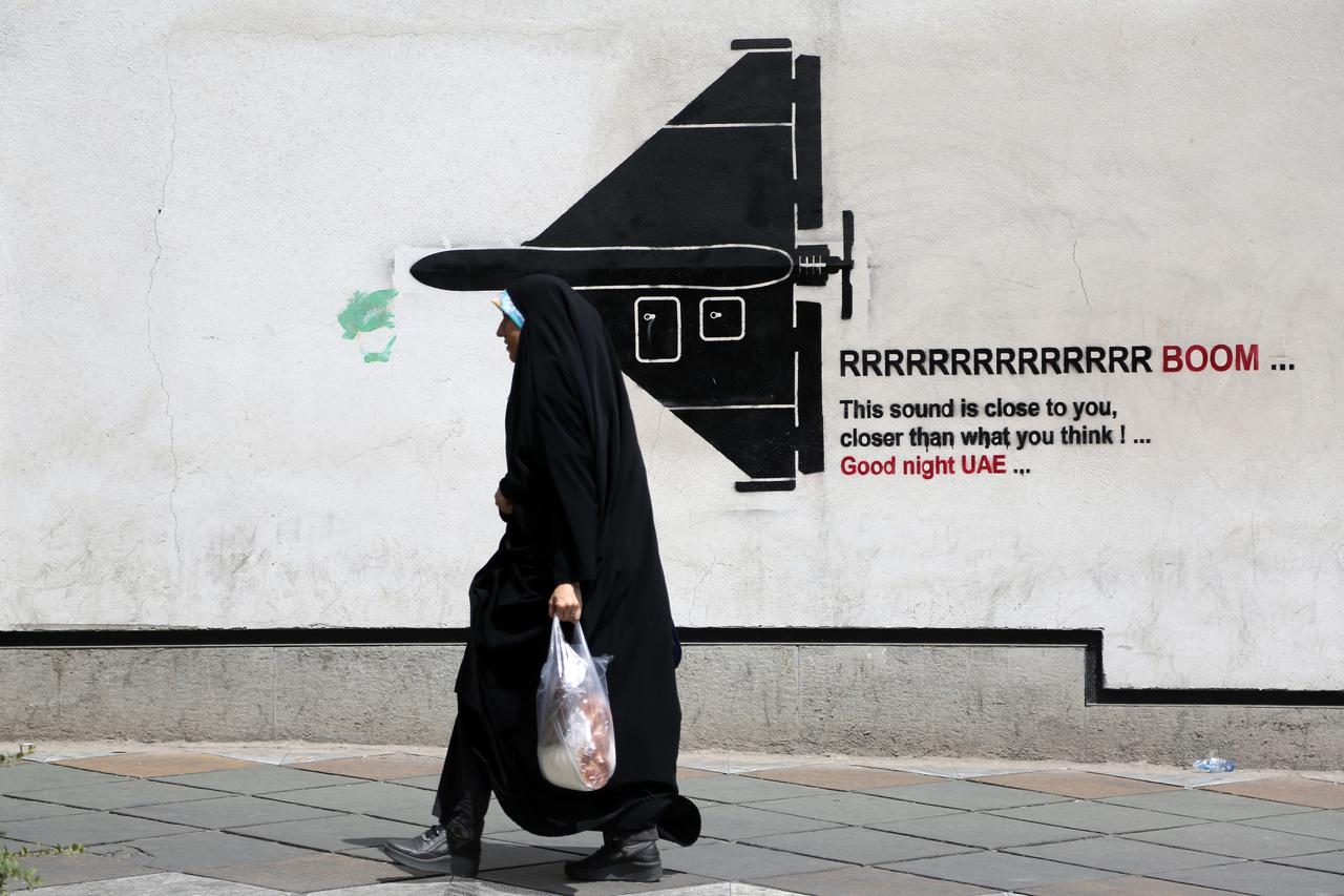 A woman walks past war-themed graffiti and murals painted on walls along the capital Tehran's streets and avenues as air defense systems are activated during the night while daily life continues in the shadow of rising military tensions between the US and Iran on July 22, 2026 in Tehran, Iran. (AA Photo)