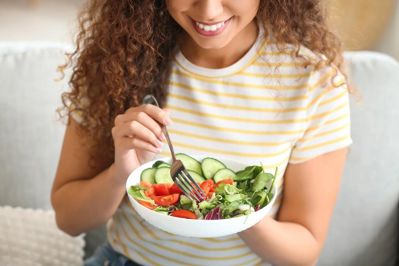 A woman eats a fresh vegetable salad at home. (Adobe Stock Photo)
