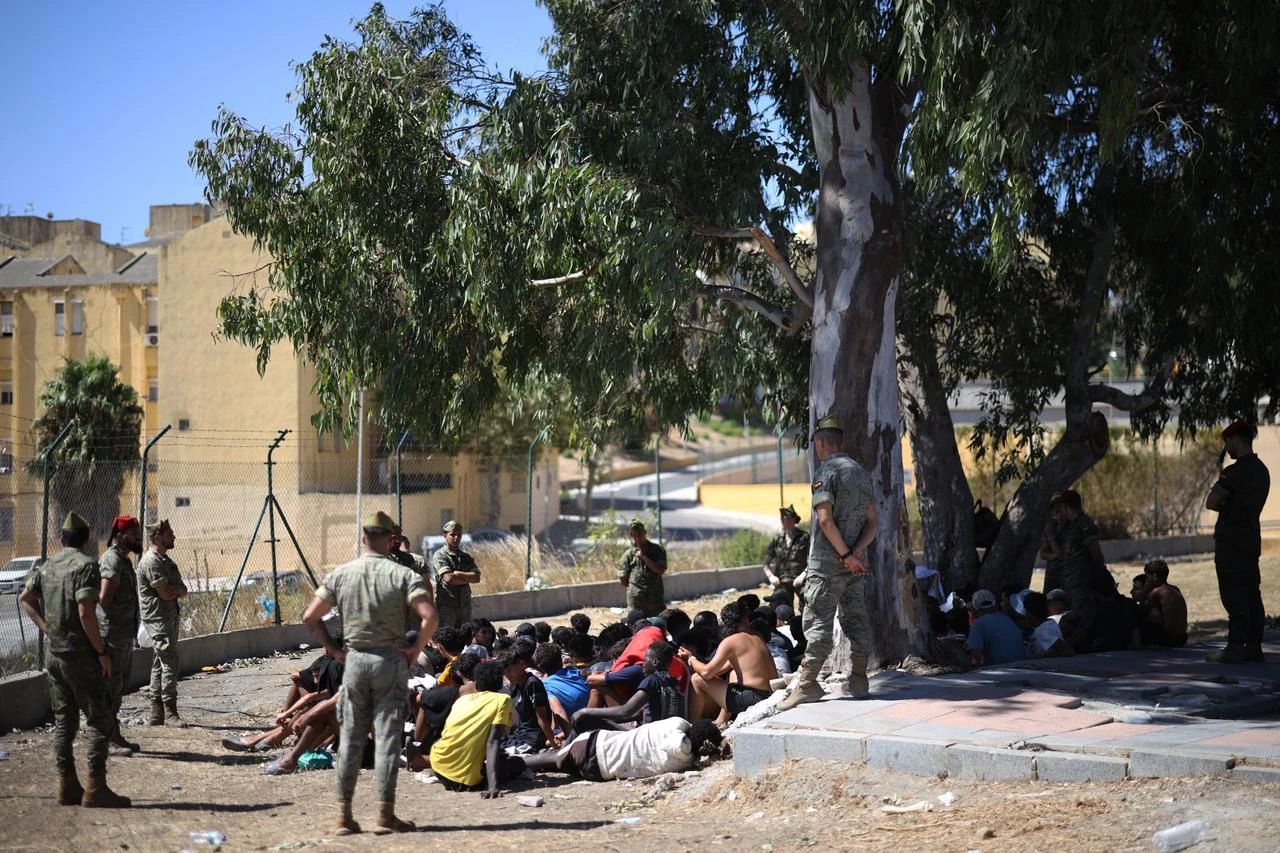 Spanish infantry soldiers watch a group of migrants sitting on the ground near the border post, prior to escorting them back to Morocco, in the Spanish enclave of Ceuta, August 2, 2026. (AFP Photo)
