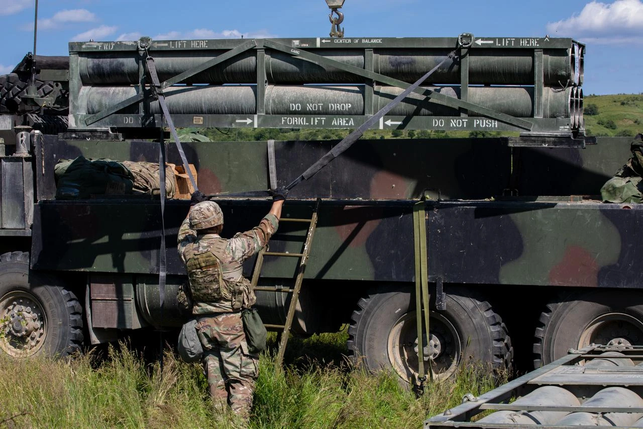 A US soldier lowers the loader launcher module of an M270A2 Multiple Launch Rocket System onto a Heavy Expanded Mobility Tactical Truck while conducting uploading and downloading procedures during Saber Guardian 25, Cincu Training Area, Romania, June 15, 2025. (Photo via US Army)
