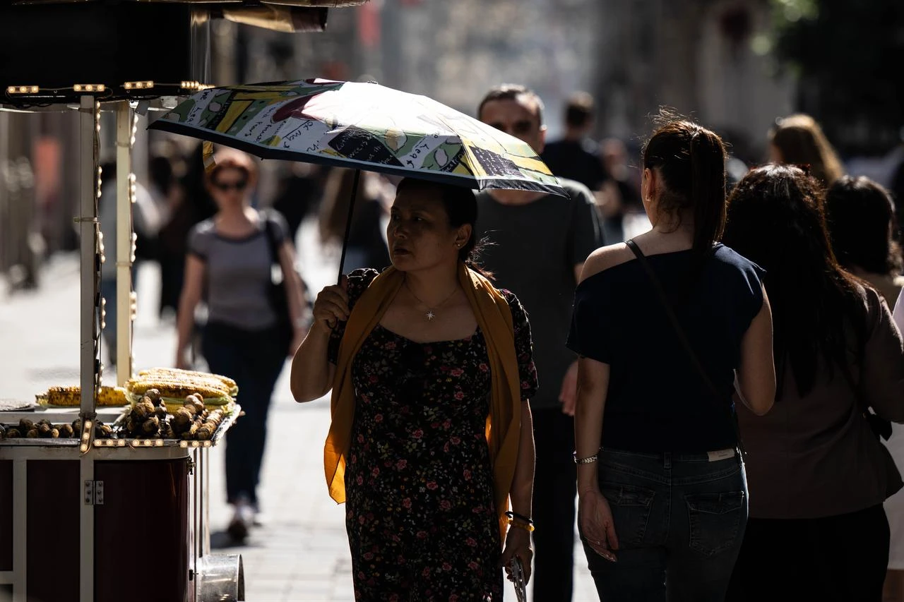 Locals and tourists use umbrellas, hats, and fans to cool off from the hot weather in Istanbul, Türkiye on July 29, 2026. (AA Photo)