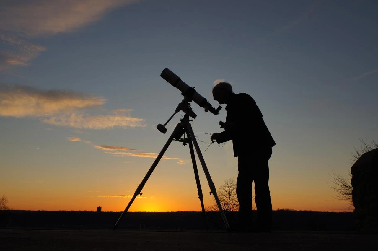 An observer uses a telescope beneath the evening sky at sunset. (Adobe Stock Photo)
