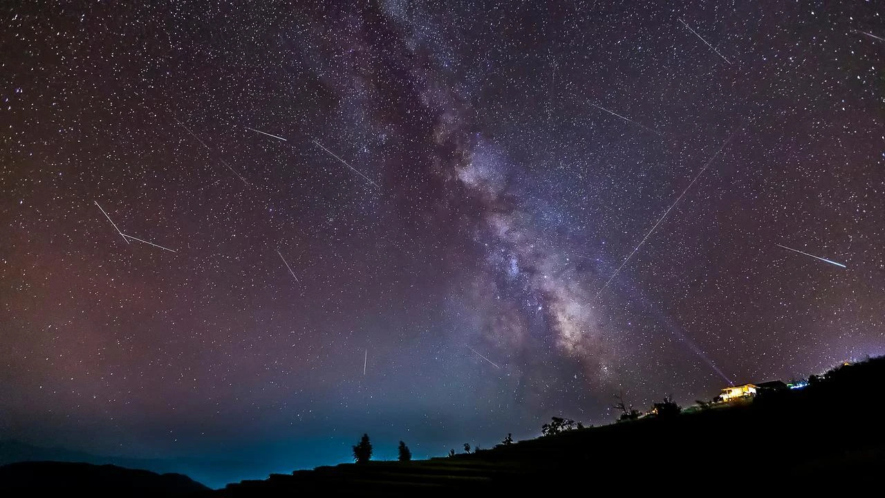 Meteors cross the Milky Way during a meteor shower over a dark rural landscape. (Adobe Stock Photo)
