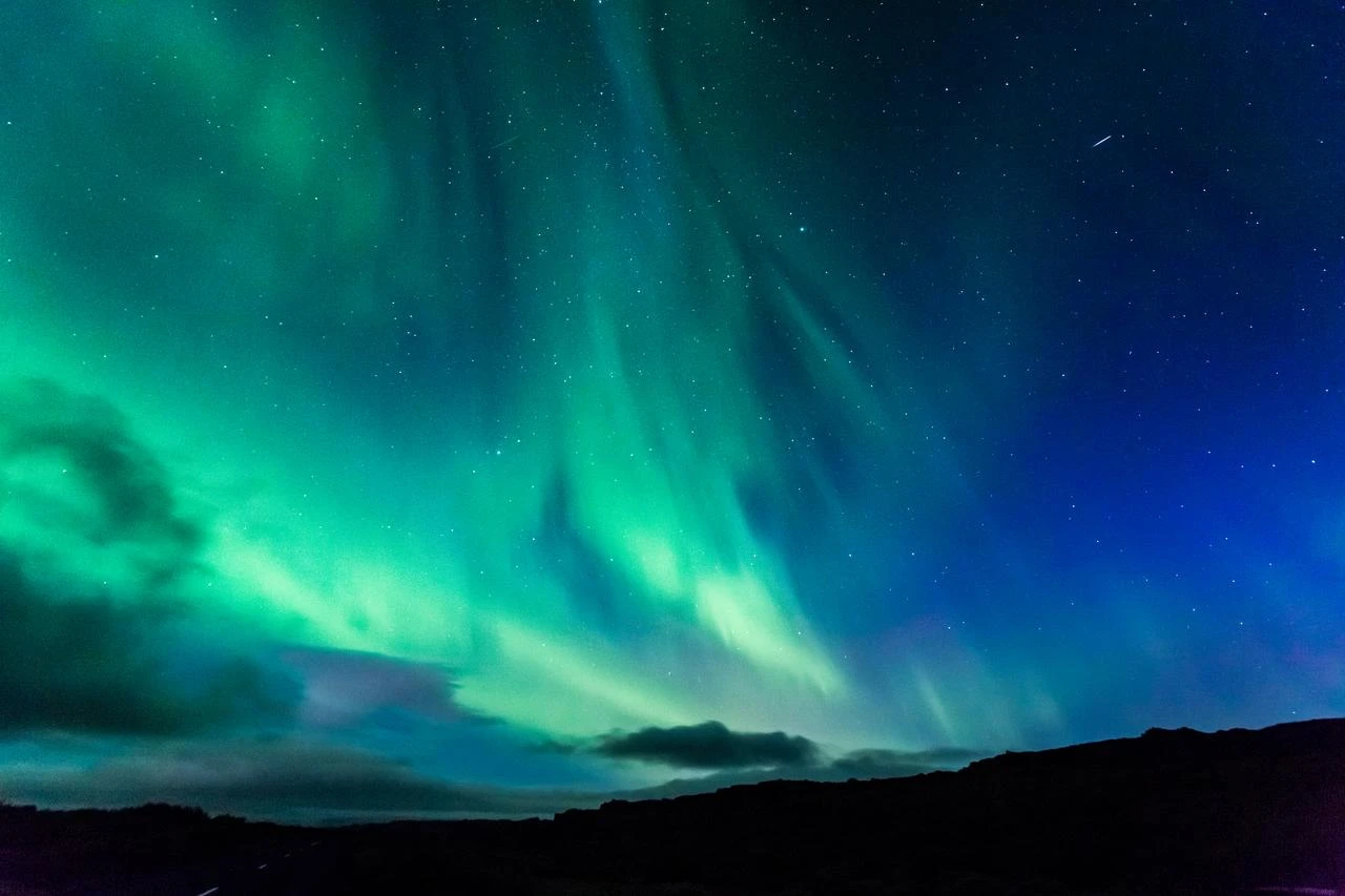 The aurora borealis illuminates the night sky above a dark mountain range. (Envato Stock Photo)
