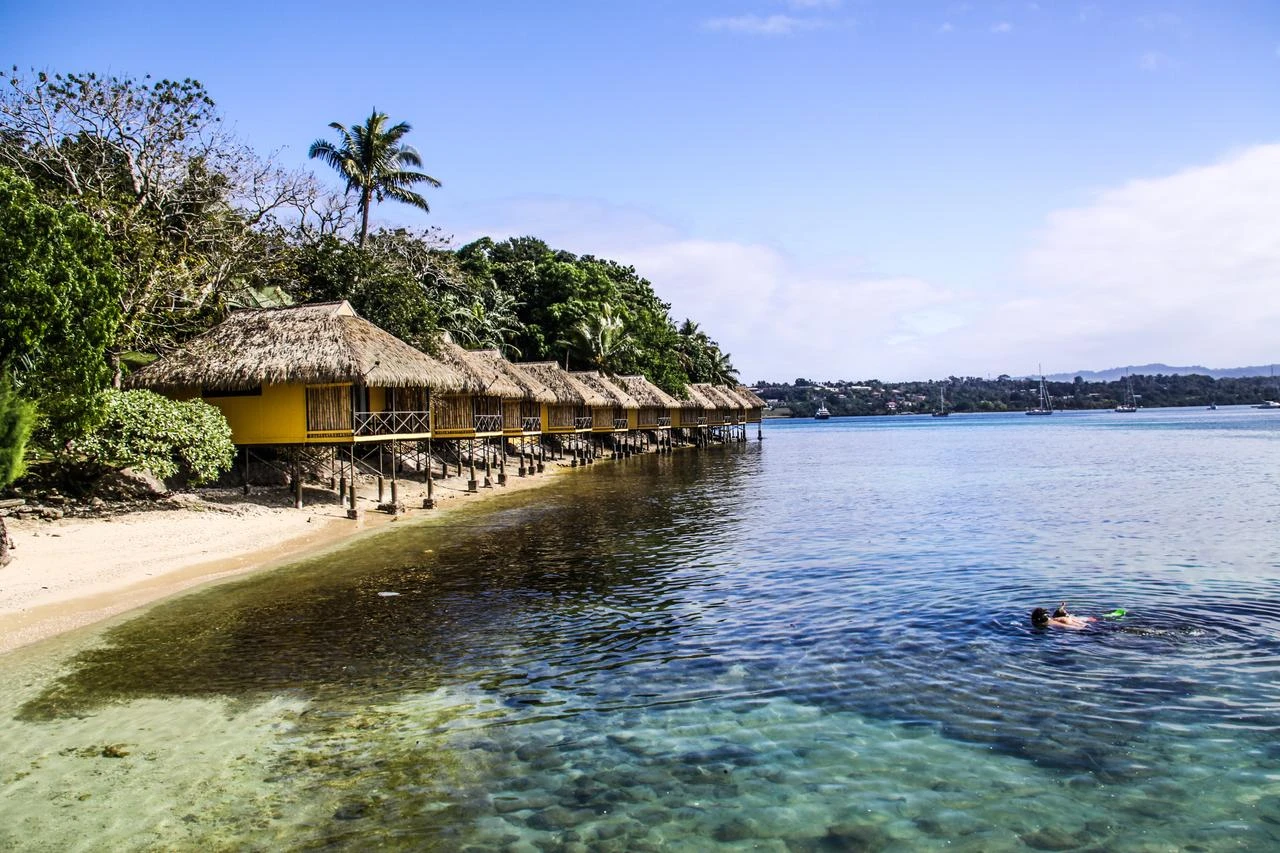 Overwater bungalows line a tropical lagoon as a visitor snorkels in the clear coastal waters. (Adobe Stock Photo)