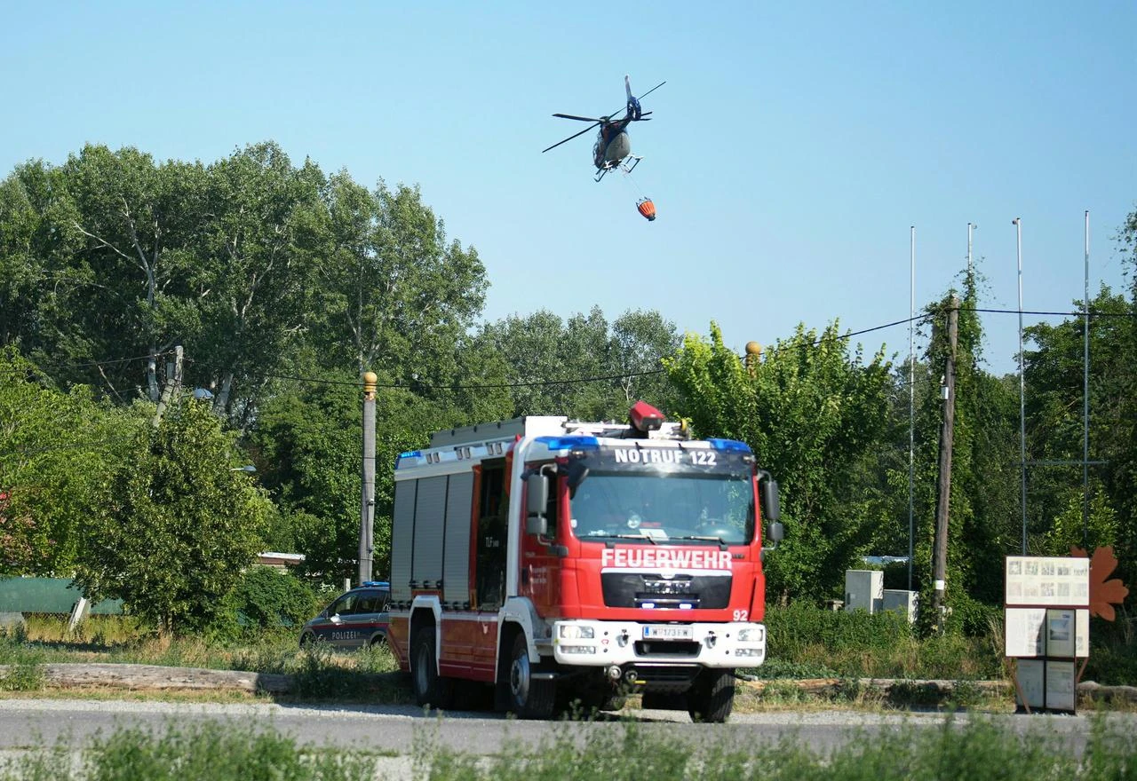 A police helicopter helping to tackle the blaze flies overhead as members of the fire brigade work near the scene of a forest fire in Vienna, Austria, on August 4, 2026. (AFP Photo)