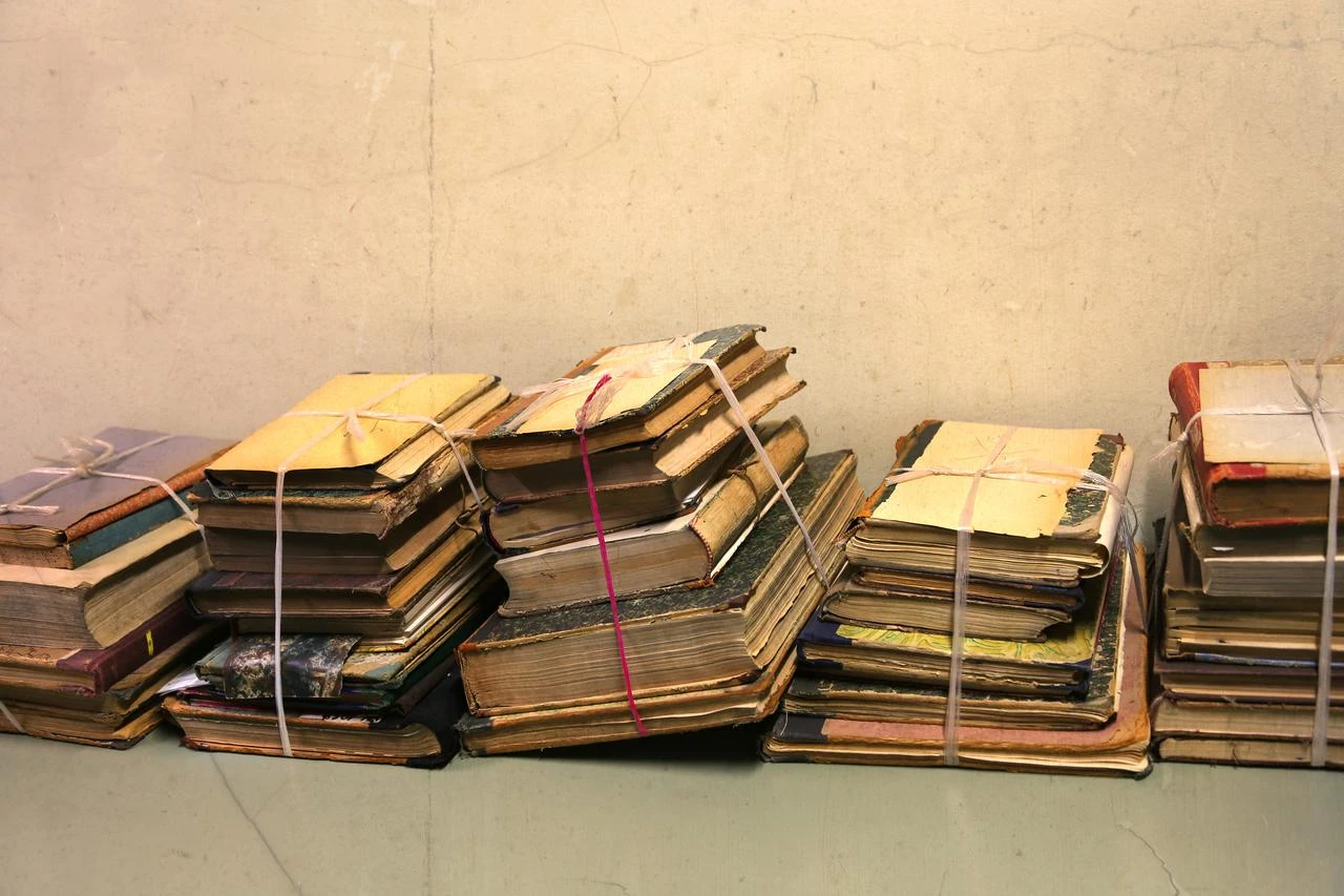 Stacks of aged books tied with string are arranged against a wall. (Envato Stock Photo)