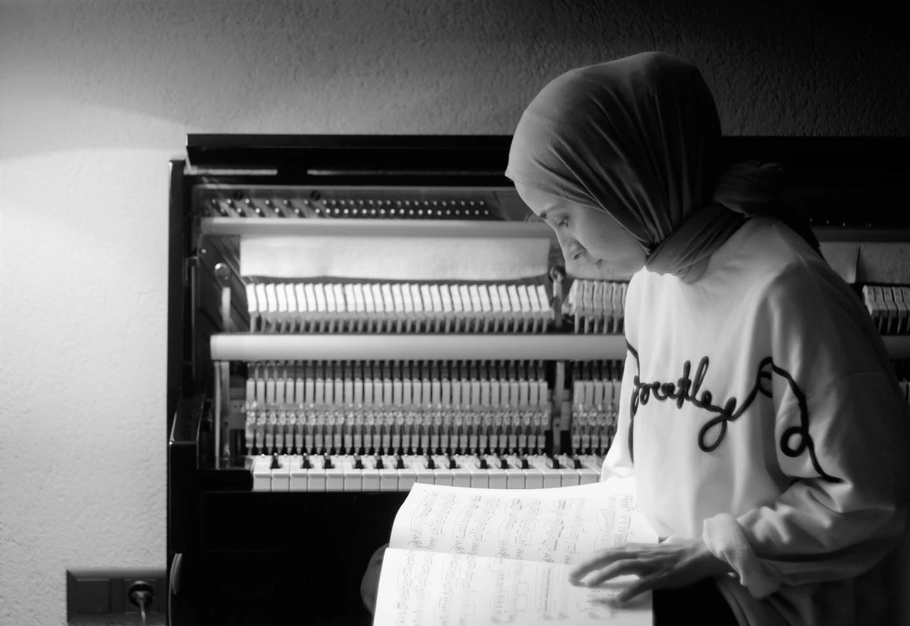 Busra Kayikci poses with a music notebook in front of her piano. (Photo via Busra Kayikci)