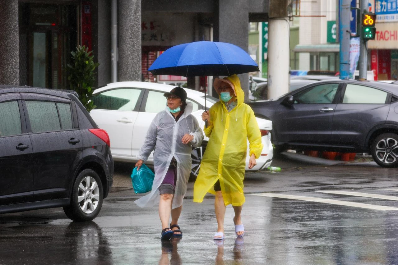 People walk under an umbrella and in raincoats amid heavy rain brought by Typhoon Dolphin in Miaoli County, Taiwan, Aug. 9, 2026. (AA Photo)