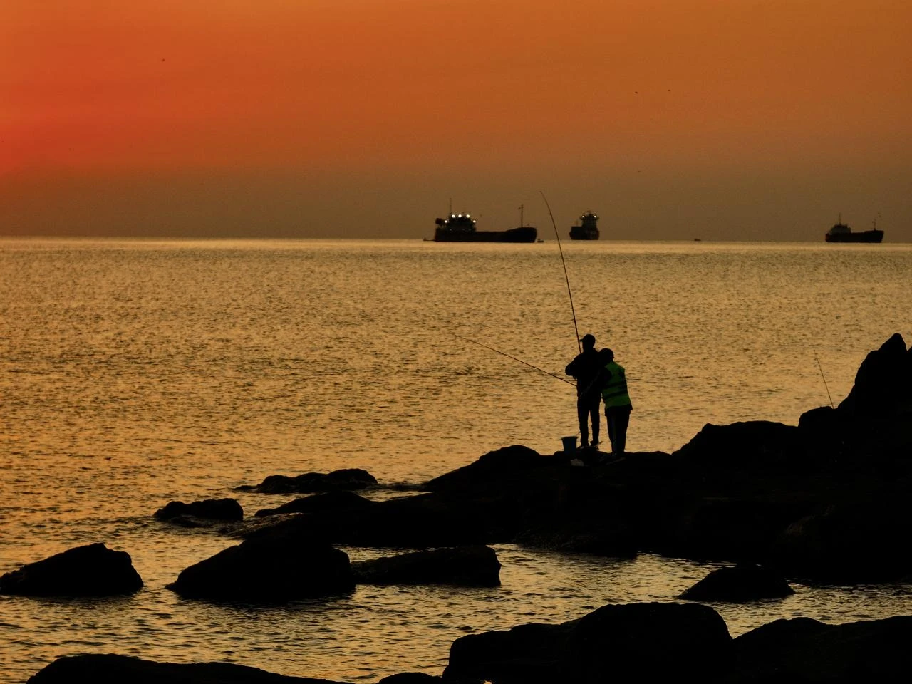 People fish along the Black Sea coast as the sky glows red during sunrise near Bati Park in the Ilkadim district of Samsun, Türkiye, on August 9, 2026. (AA Photo)