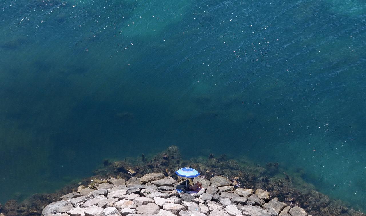 A sunbather rests beneath an umbrella on rocks beside the sea during hot summer weather, in a file photo. (AFP Photo)