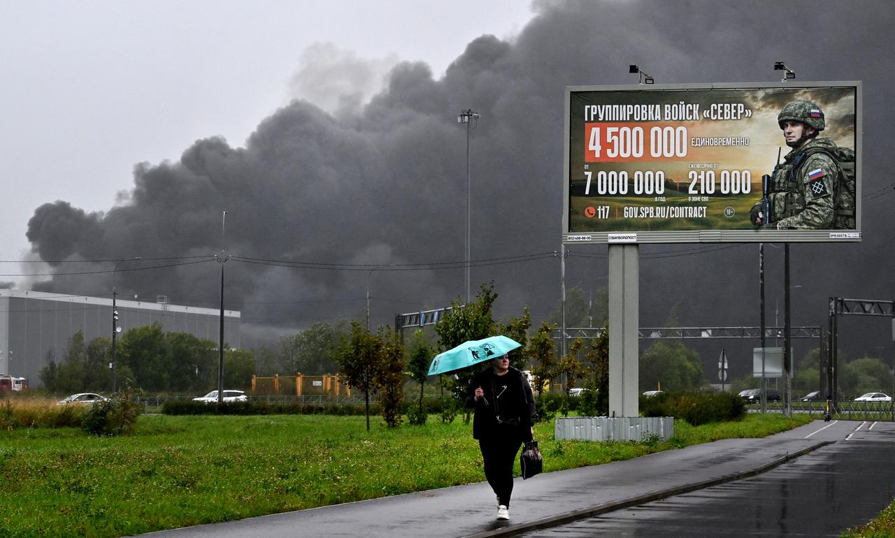 Smoke rises over a logistics center in Kolpino, outside Saint Petersburg behind a billboard promoting contract army service after being hit by Ukrainian drones early on August 23, 2026. (AFP Photo)