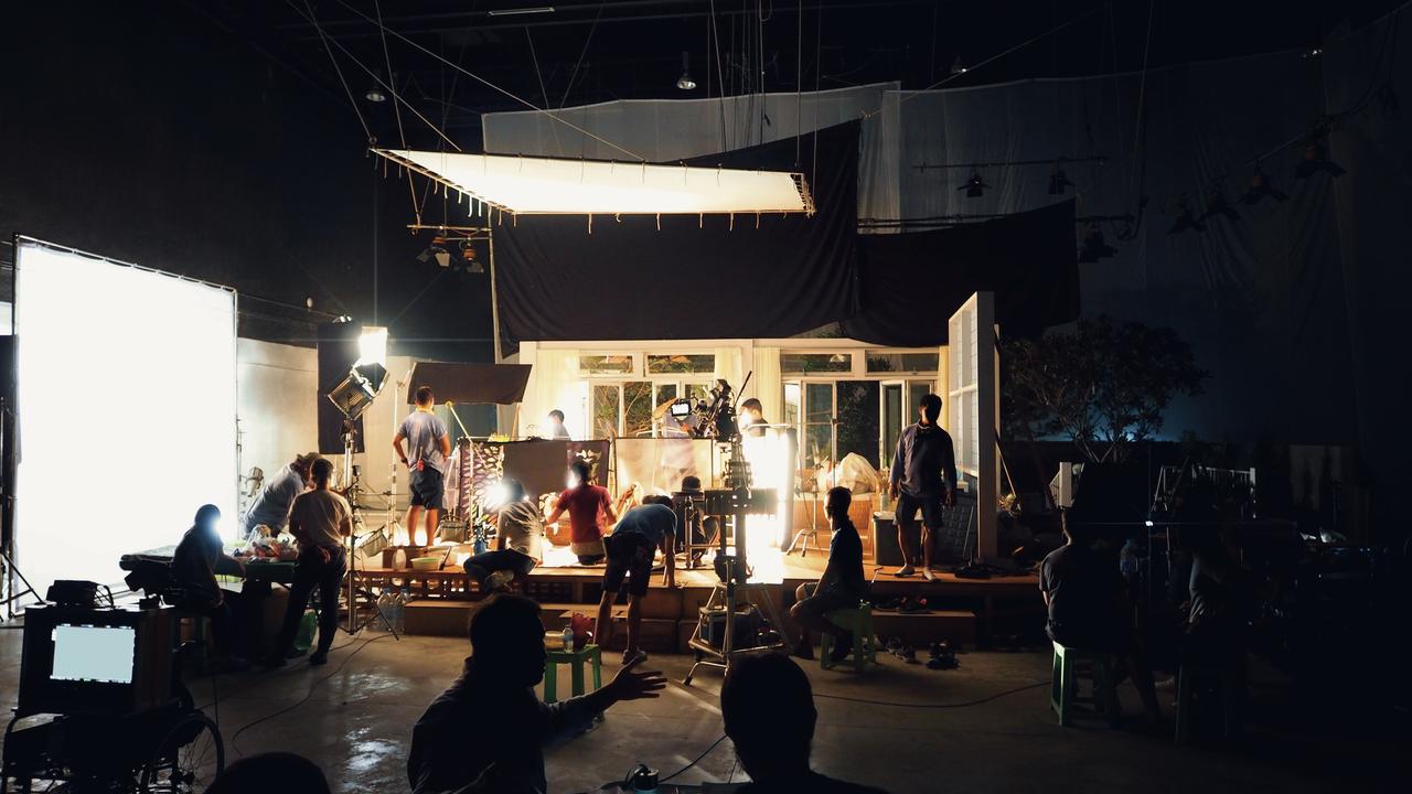 A film crew works around a brightly lit set inside a production studio, illustrating the behind-the-scenes process of television and film production. (Adobe Stock Photo)