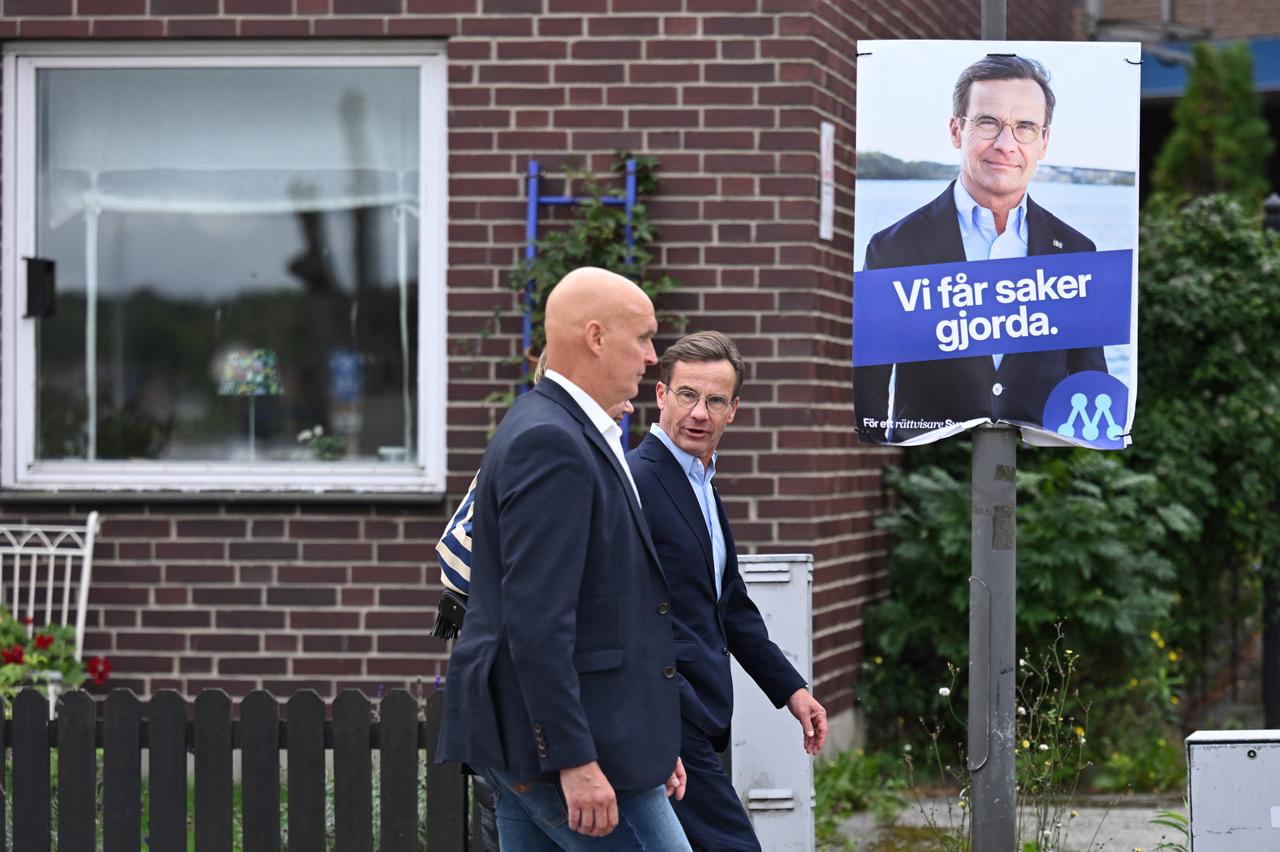 Sweden's Prime Minister Ulf Kristersson (R) walks past one of his election posters as he arrives at a polling station on Sept. 13, 2026. (AFP Photo)