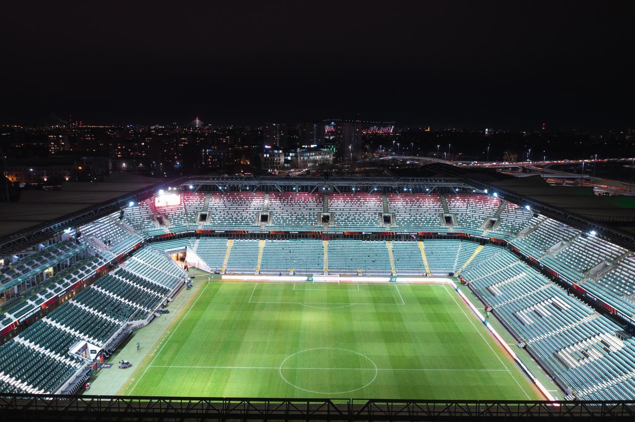 An illuminated football stadium stands empty at night with UEFA Europa League branding visible around the stands. (Adobe Stock Photo)