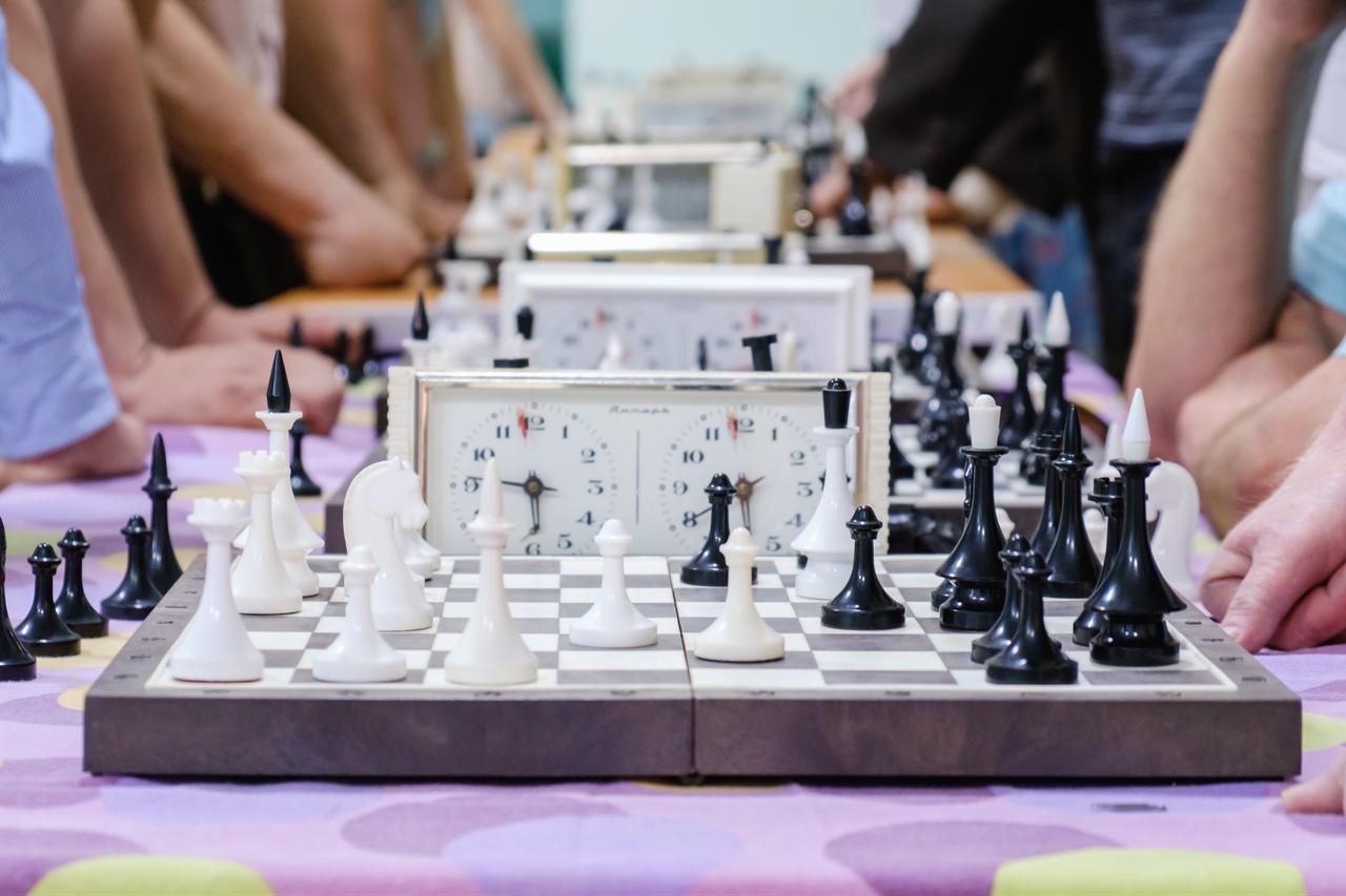 Chess players compete across multiple boards during a timed tournament, with analog chess clocks positioned beside the games. (Adobe Stock Photo)