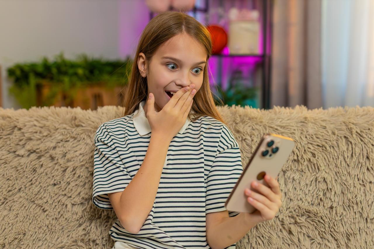 A young girl reacts while looking at a smartphone, illustrating social media, online trends and digital communication. (Adobe Stock Photo)