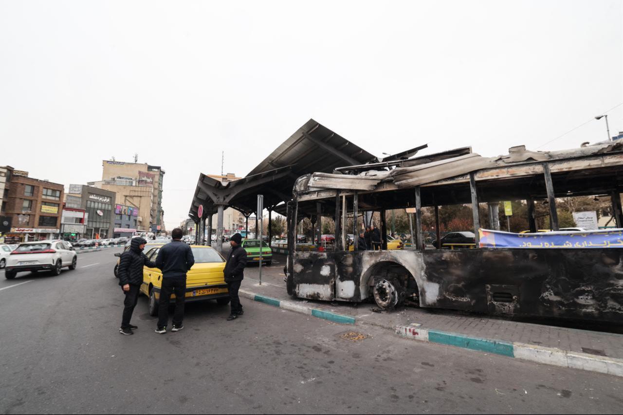 A photograph shows the wreckage of a burnt bus bearing a banner that reads "This was one of Tehran’s new buses that was paid for with the money of the people’s taxes,” in Tehran's Sadeghieh Square on January 15, 2026. (AFP Photo)