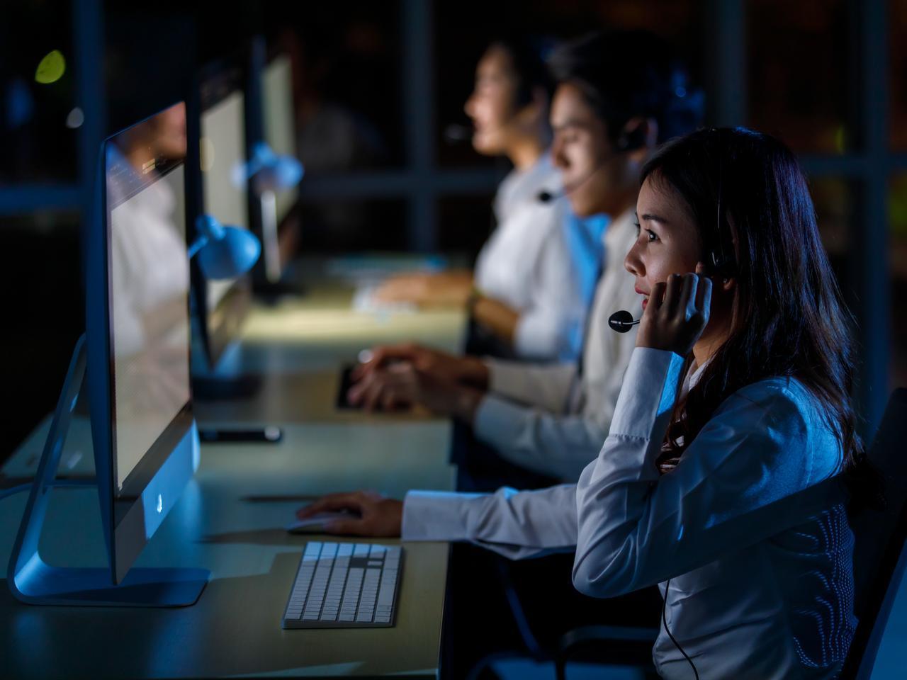 The photo shows an operator wearing headphones, helping a customer online in a call center office at night, at an unspecified location and time. (Adobe Stock Photo)