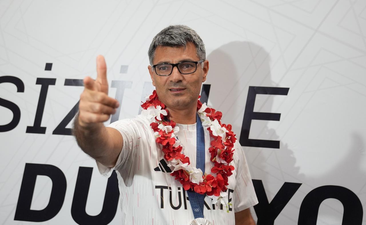 Yusuf Dikec, adorned with a victory garland and his silver medal, strikes his viral pose after returning to Türkiye, following his success in the mixed team 10-meter air pistol event at the Paris 2024 Olympic Games, in Istanbul Airport, Türkiye, on Aug. 1, 2024. (AA Photo)