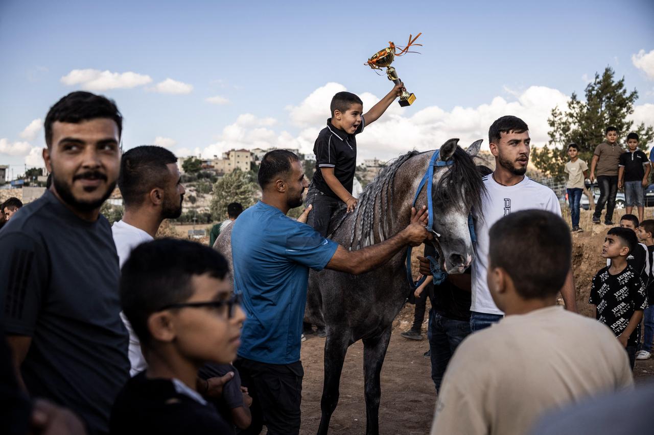 A young Palestinian boy holds up a trophy as he sits on his family's winning horse during a local horse race in al-Majd, west of the Israeli-occupied West Bank city of Hebron on Sept. 18, 2026. (AFP Photo)