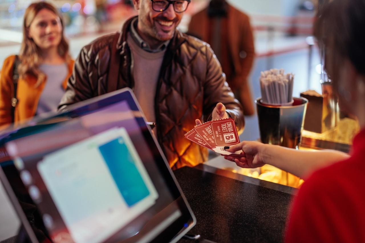 A moviegoer hands cinema tickets to a staff member at a theater counter. (Adobe Stock Photo)
