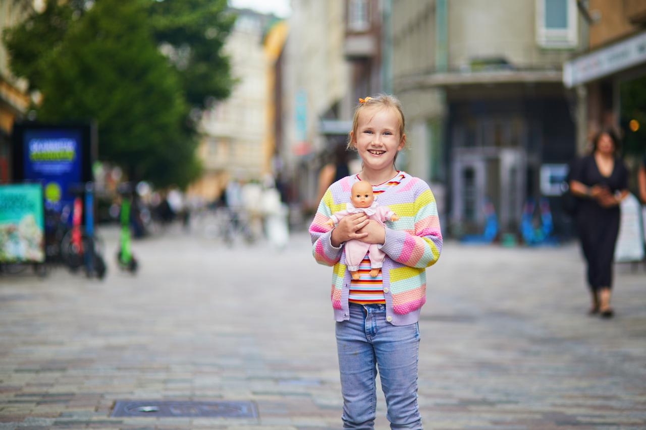 Happy young girl holding a baby doll on a pedestrian street in Helsinki, Finland. (Adobe Stock Photo)