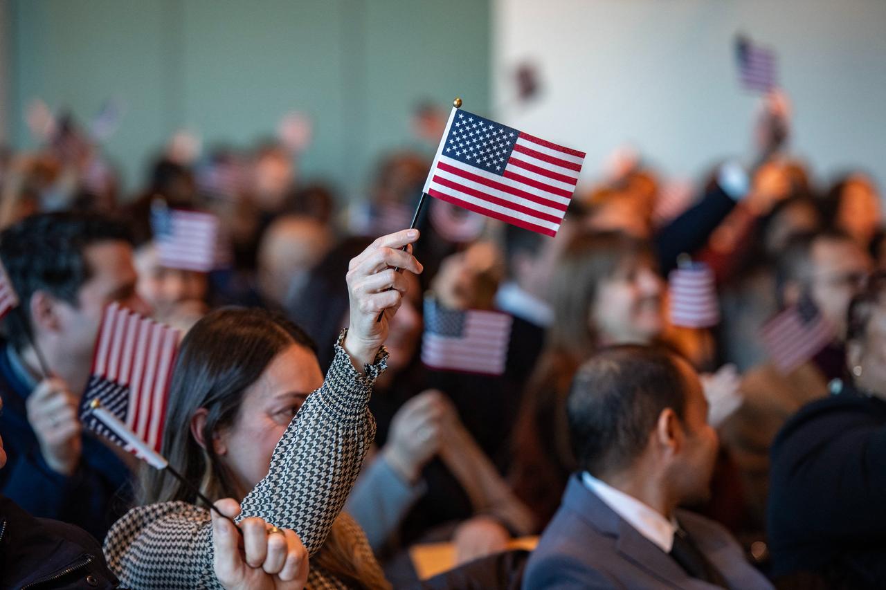 People wave US flags to celebrate becoming US citizens after taking the oath of allegiance during a naturalization ceremony in the jury assembly room at the John Joseph Moakley United States Courthouse in Boston, Massachusetts on January 8, 2025. (AFP Photo)