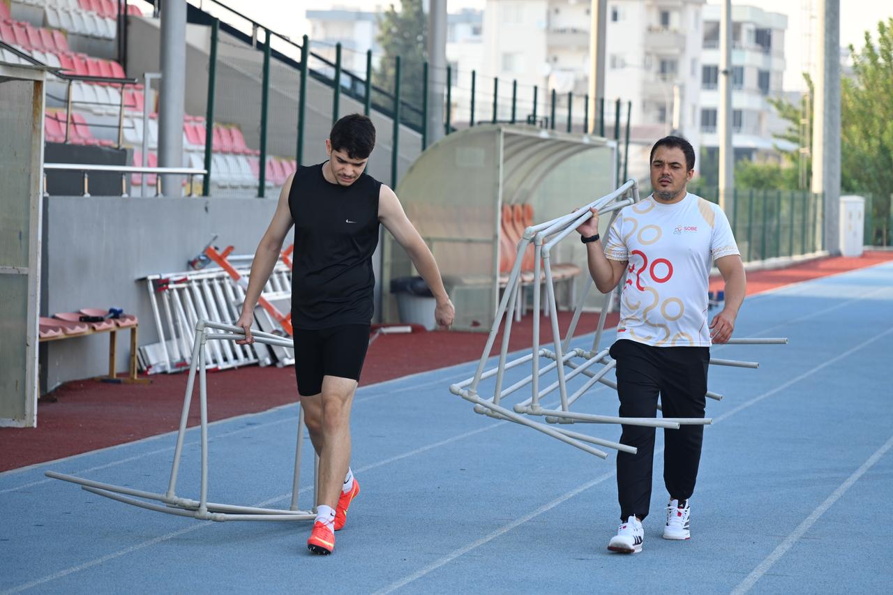 Athlete Ozgur Salih Kose and his coach Nuri Can Kastal carrying training equipment together across the running track. (AA Photo)