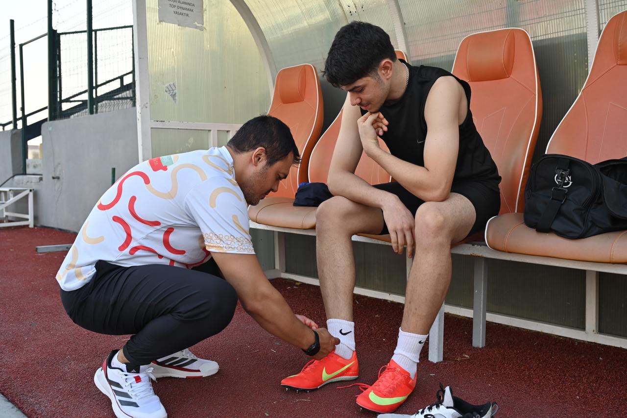 Coach Nuri Can Kastal helps tie the running shoe of 17-year-old national athlete Ozgur Salih Kose on a bench at the athletic track. (AA Photo)