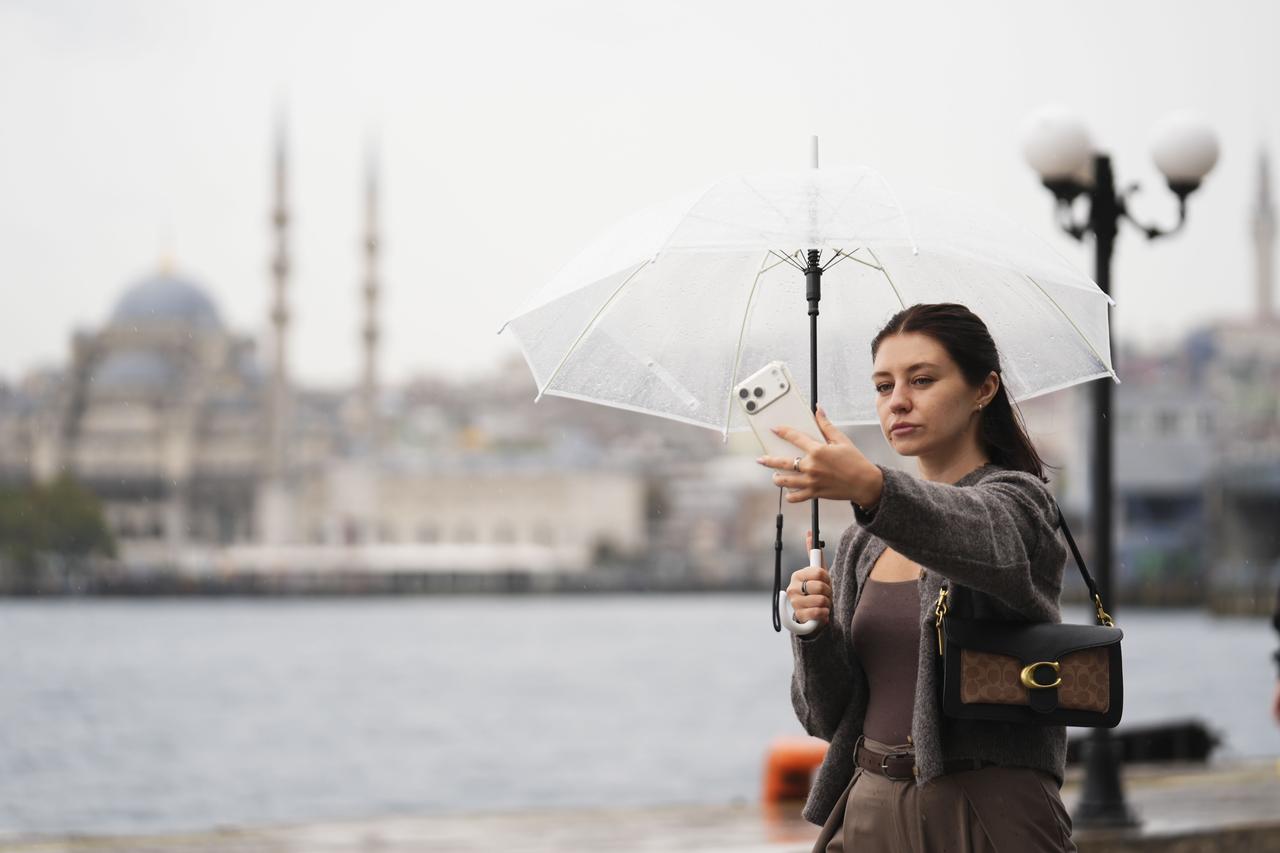 Woman holding a clear umbrella and taking a selfie with her phone outdoors in Karakoy, Istanbul. (AA Photo)