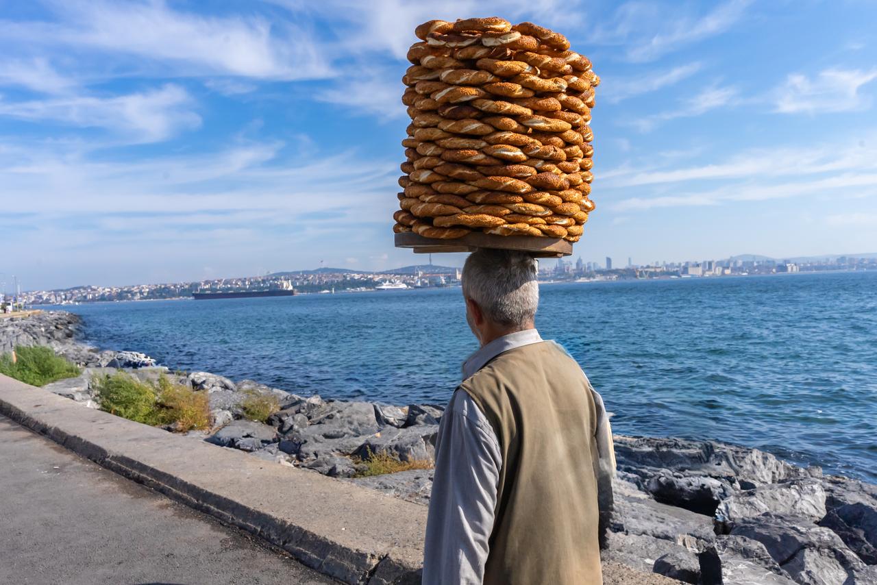 A simit vendor carries a large stack of the sesame-covered bread rings along Istanbul's waterfront, Türkiye. (Adobe Stock Photo)
