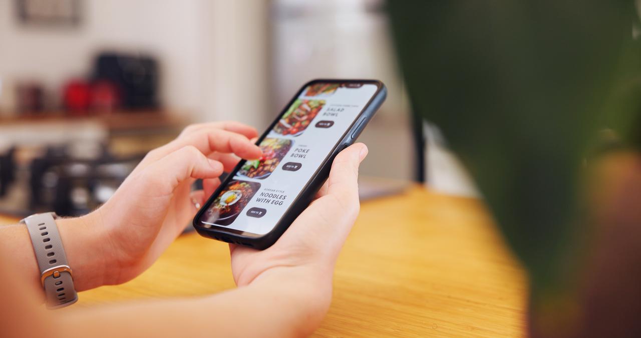 A person uses a smartphone to browse an online food-ordering platform. (Adobe Stock Photo)