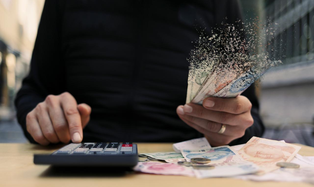 A person uses a calculator while holding Turkish lira banknotes, illustrating inflation and declining purchasing power. (Adobe Stock Photo)